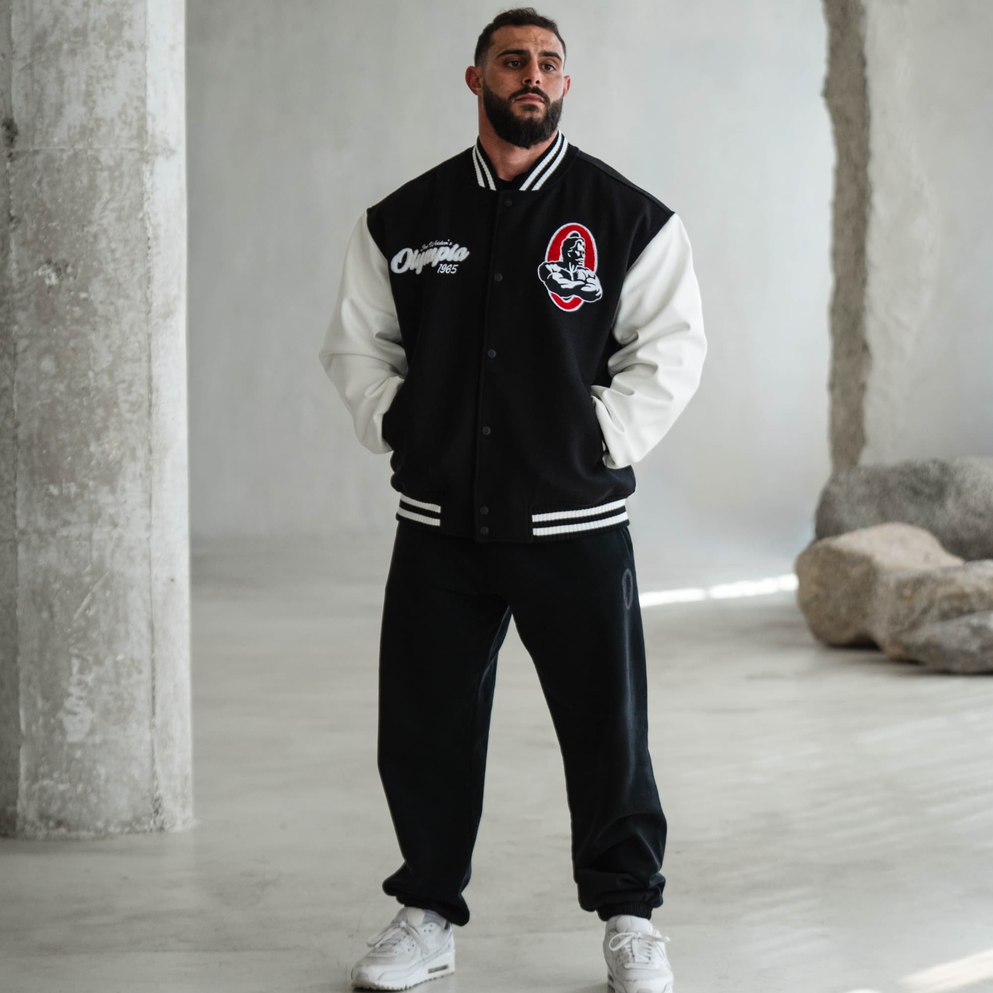 Model wearing Mr. O Varsity Jacket, front view with embroidered chest logos, styled with black pants and white shoes.