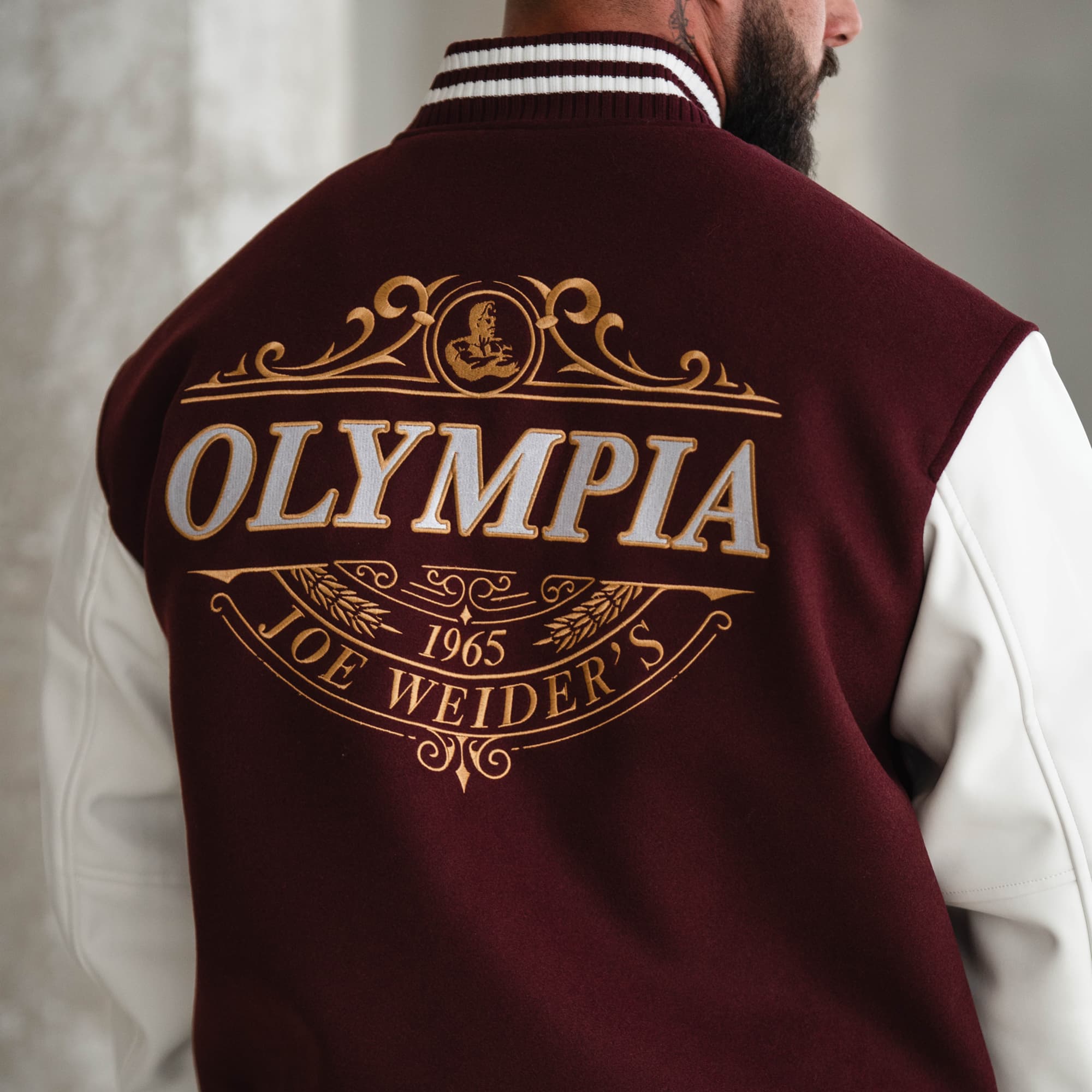 Close-up back shot of the gold Olympia crest embroidery on the Royal O Varsity Jacket with detailed stitching.