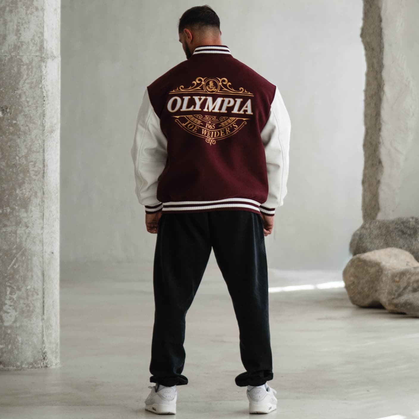 Lifestyle back view of model wearing the Royal O Varsity Jacket, showcasing the bold embroidered Olympia crest design.