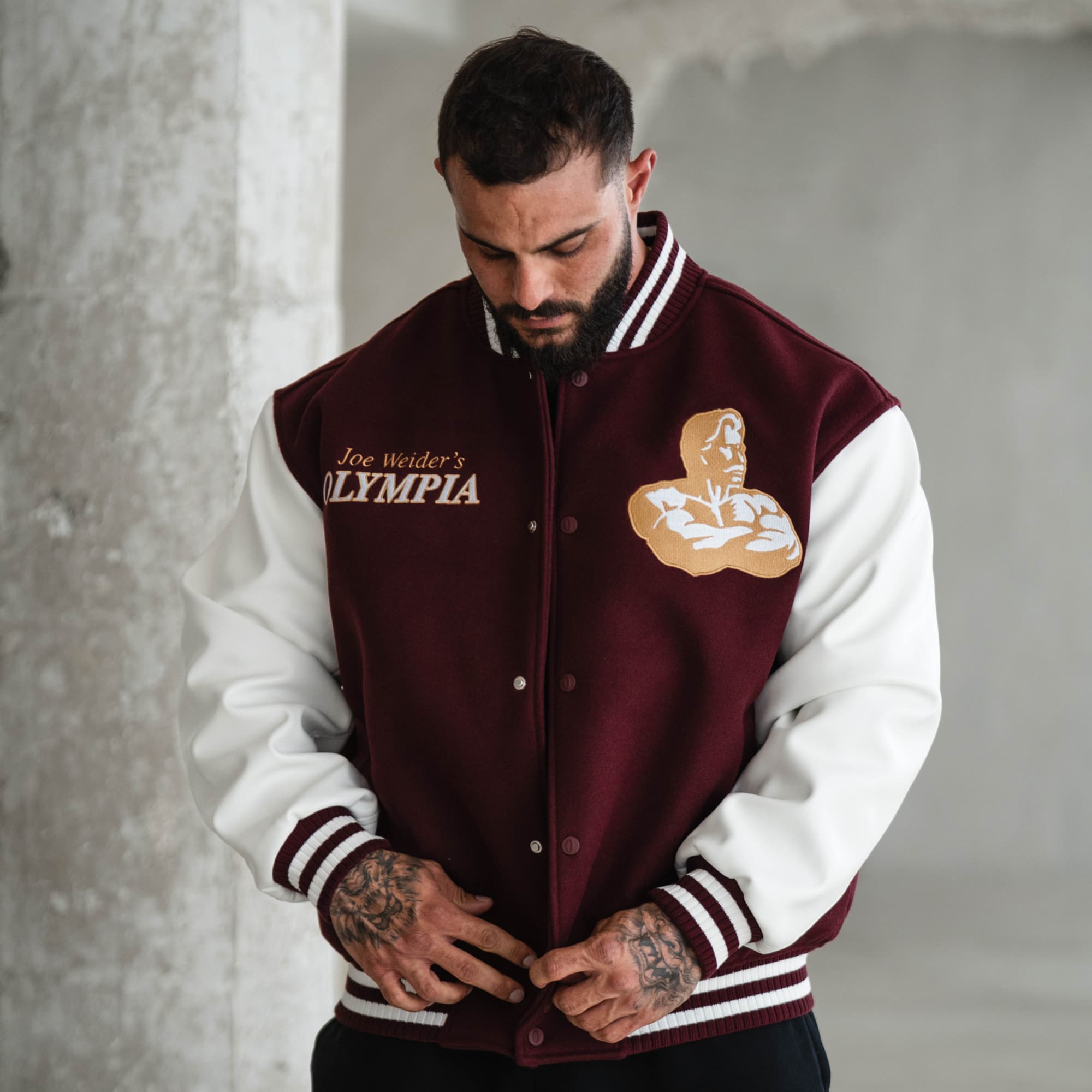 Lifestyle front shot of model adjusting burgundy snap buttons on the Royal O Varsity Jacket, highlighting chest embroidery and striped cuffs.