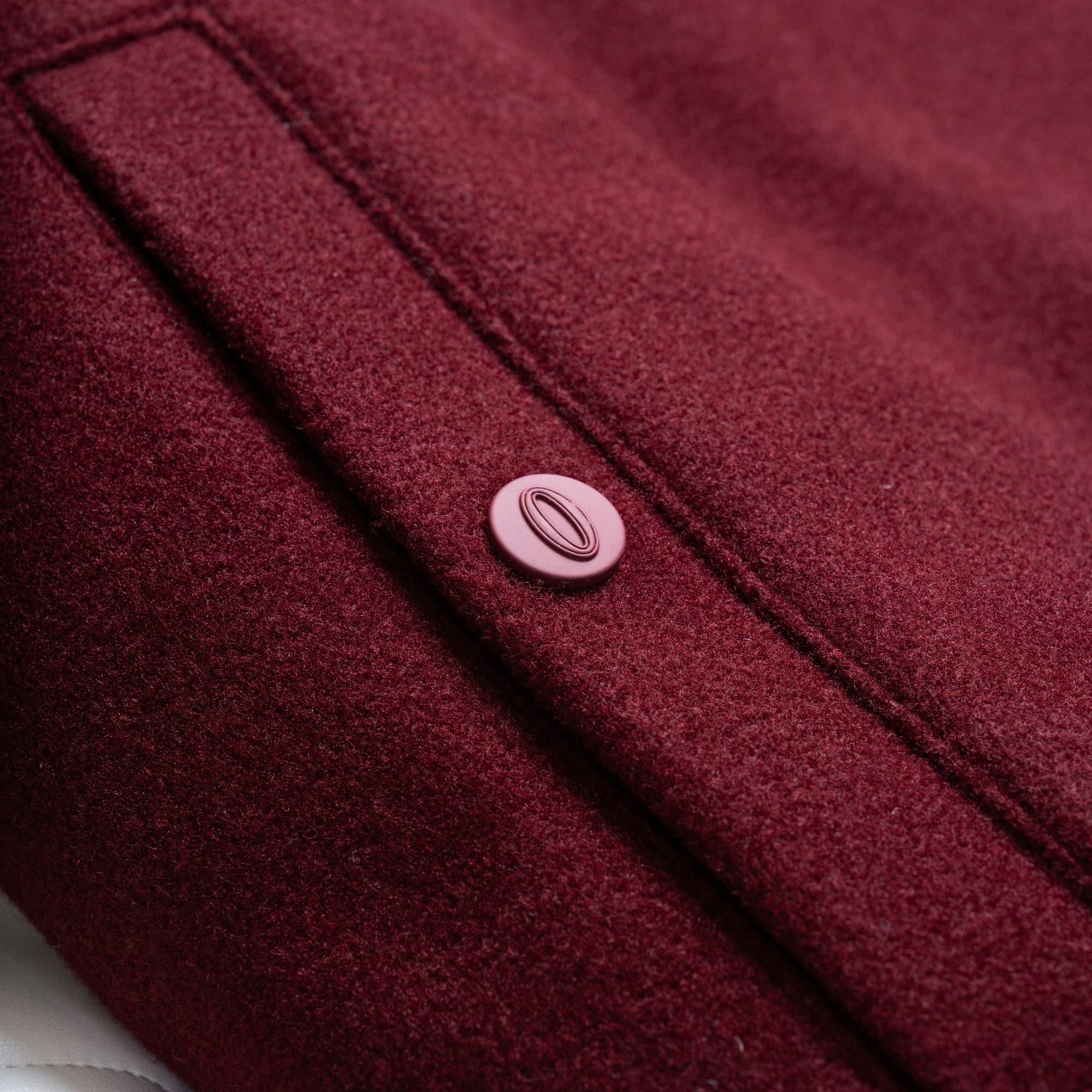 Detail shot of burgundy snap button and welt pocket on the Royal O Varsity Jacket.