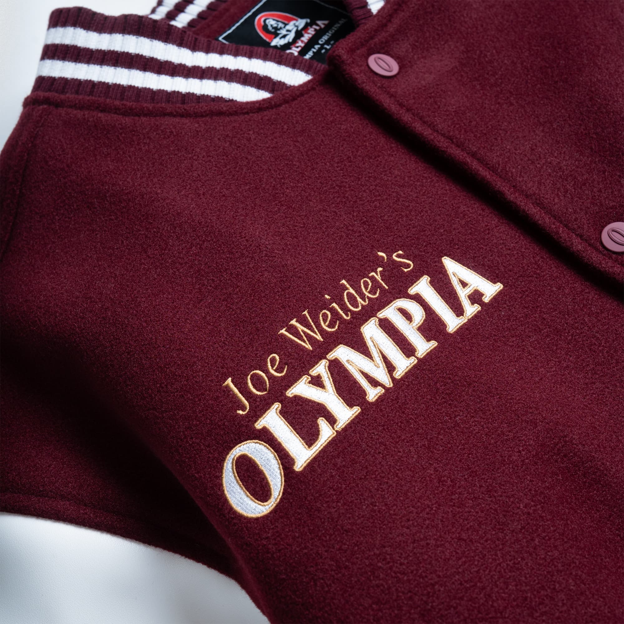 Close-up of the gold “Joe Weider’s Olympia” embroidery on the burgundy wool fabric near the collar.