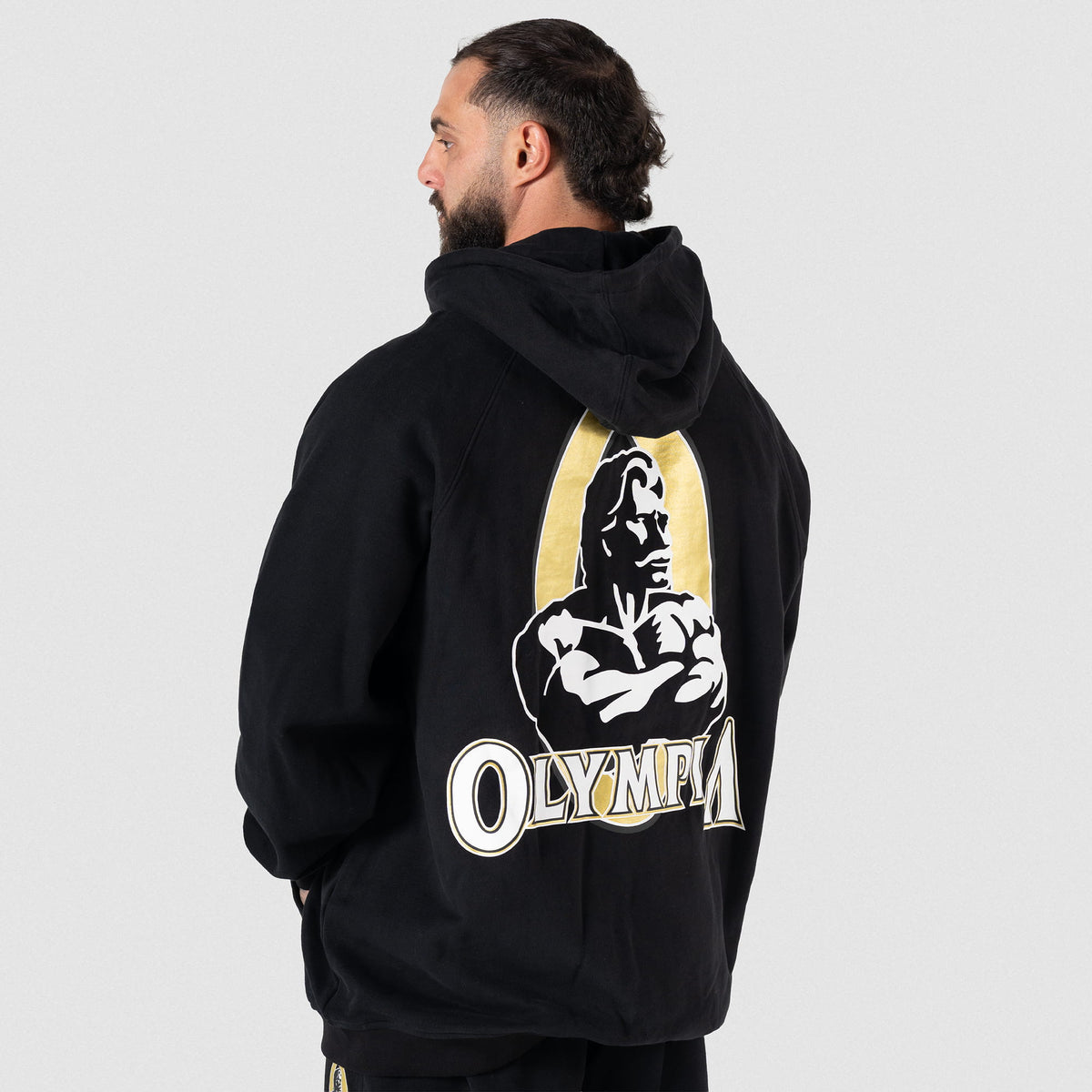 Champions Gold Zip-Up Hoodie | Male model facing away while wearing the oversized Olympia hoodie, showcasing the large gold and white back graphic
