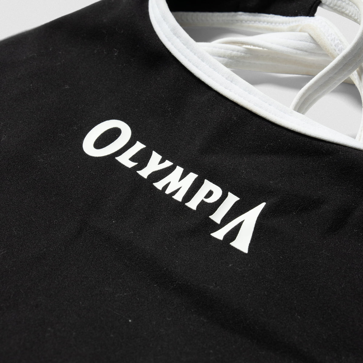 Close up of the "OLYMPIA" wordmark logo across the chest of the Olympia High Neck Bra for Women