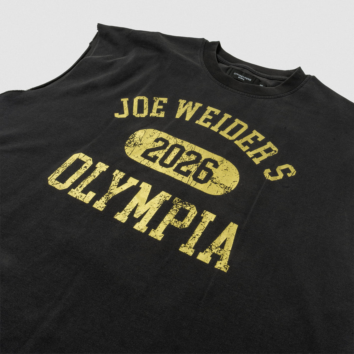 Close up view of front logo on the black Joes Olympia Cut-Off that says "Joe Weiders" in arching text, above 
"2026" in a circle, and "OLYMPIA" wordmark text below 