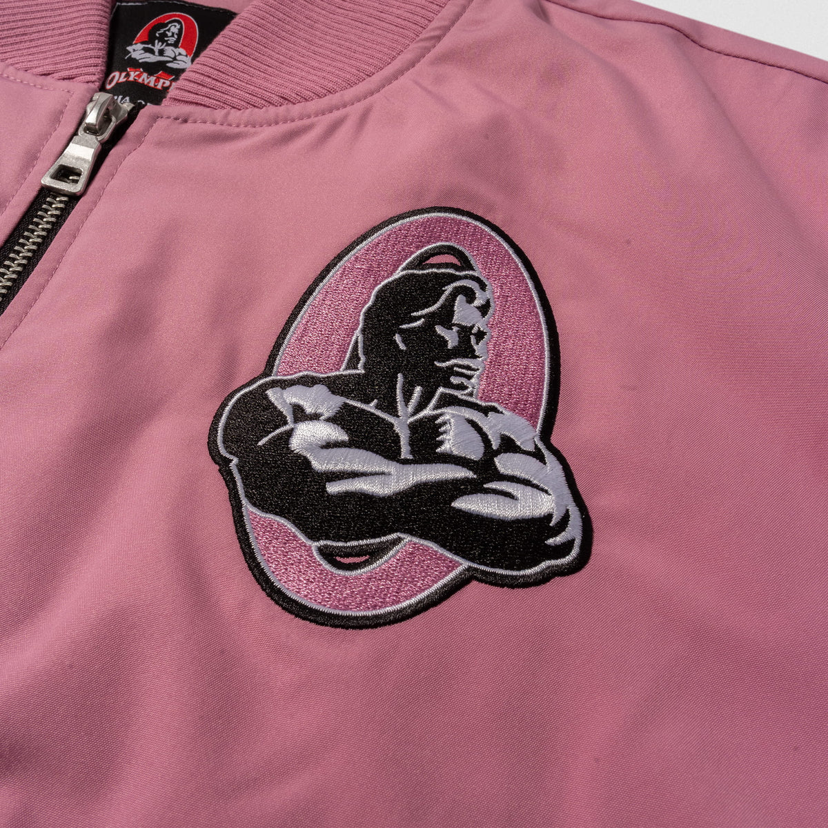Rose Division Crop Bomber Jacket | Front left chest logo of the Classic Olympia bodybuilding logo in pink and white