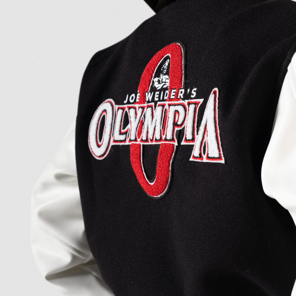 Signature Crop Varsity Jacket | Angled side view of large back graphic that says "Joe Weider's Olympia" in white with red border, overlapping an larger red "O"