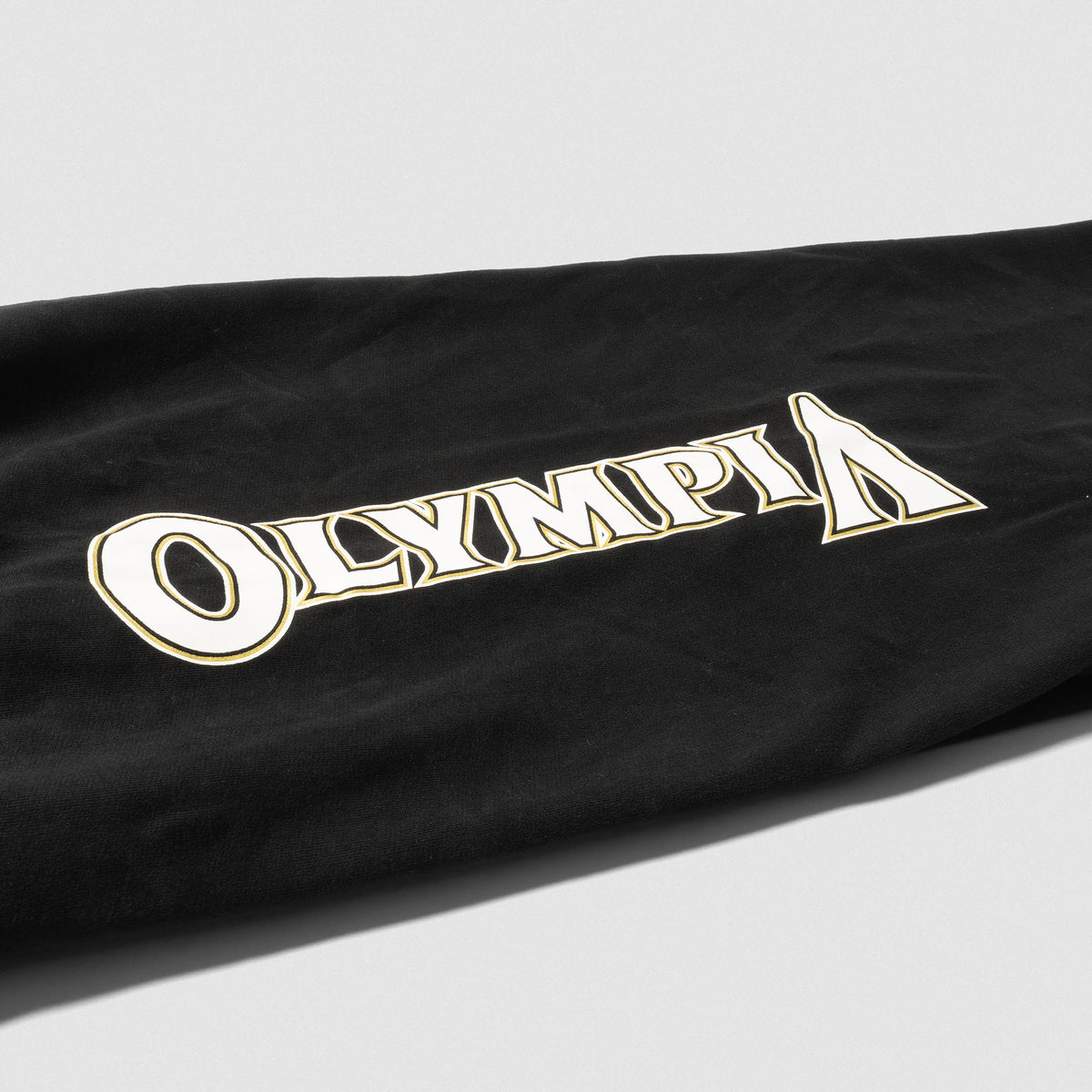 Close up of "OLYMPIA" wordmark logo found down the pantleg of the women's  Champions Gold Wide-Leg Jogger