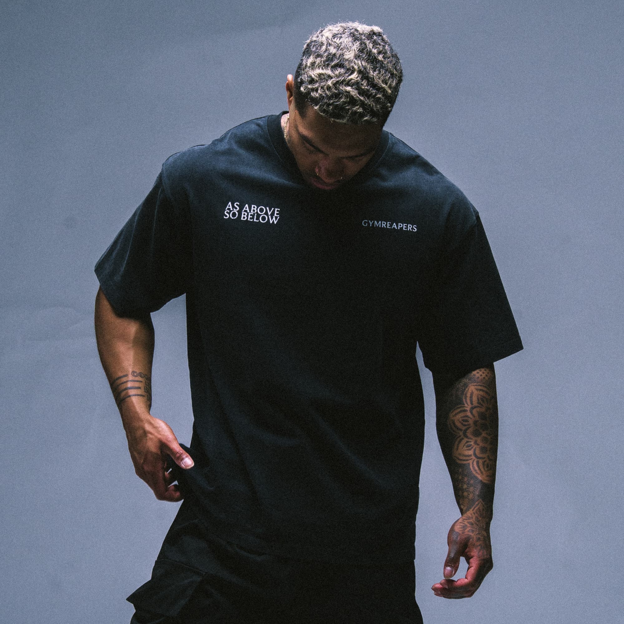 Model wearing the As Above So Below Graphic Tee in black, showcasing the minimalist front chest logos.