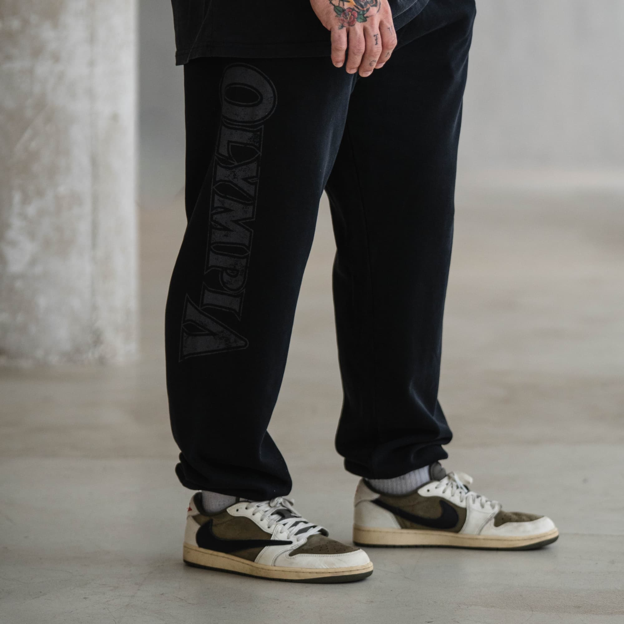 Male athlete wearing black Olympia joggers with vertical logo down right leg