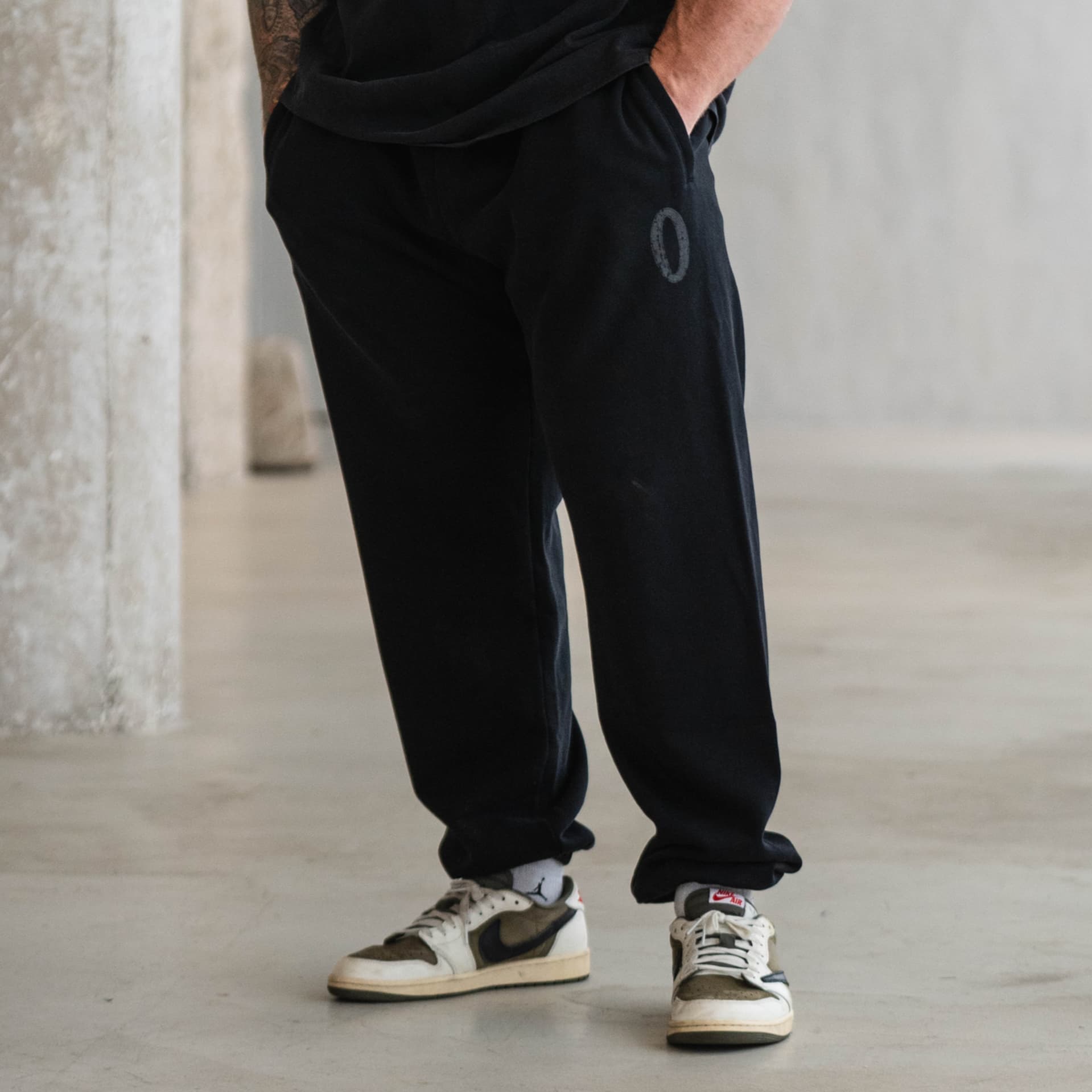 Male athlete wearing black Olympia joggers with “O” logo on hip