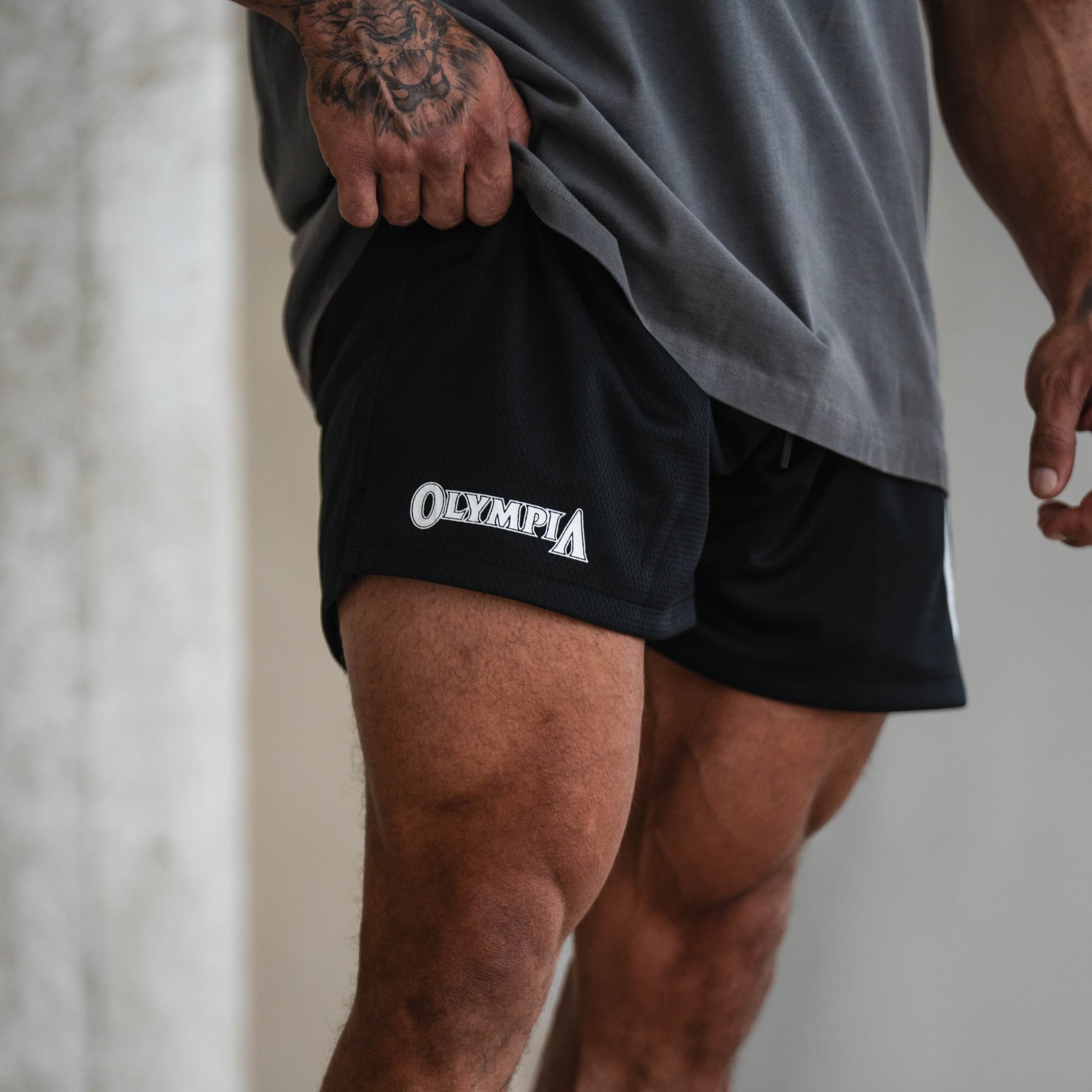 Side view of black Olympia O Mesh Shorts with Olympia logo, modeled.