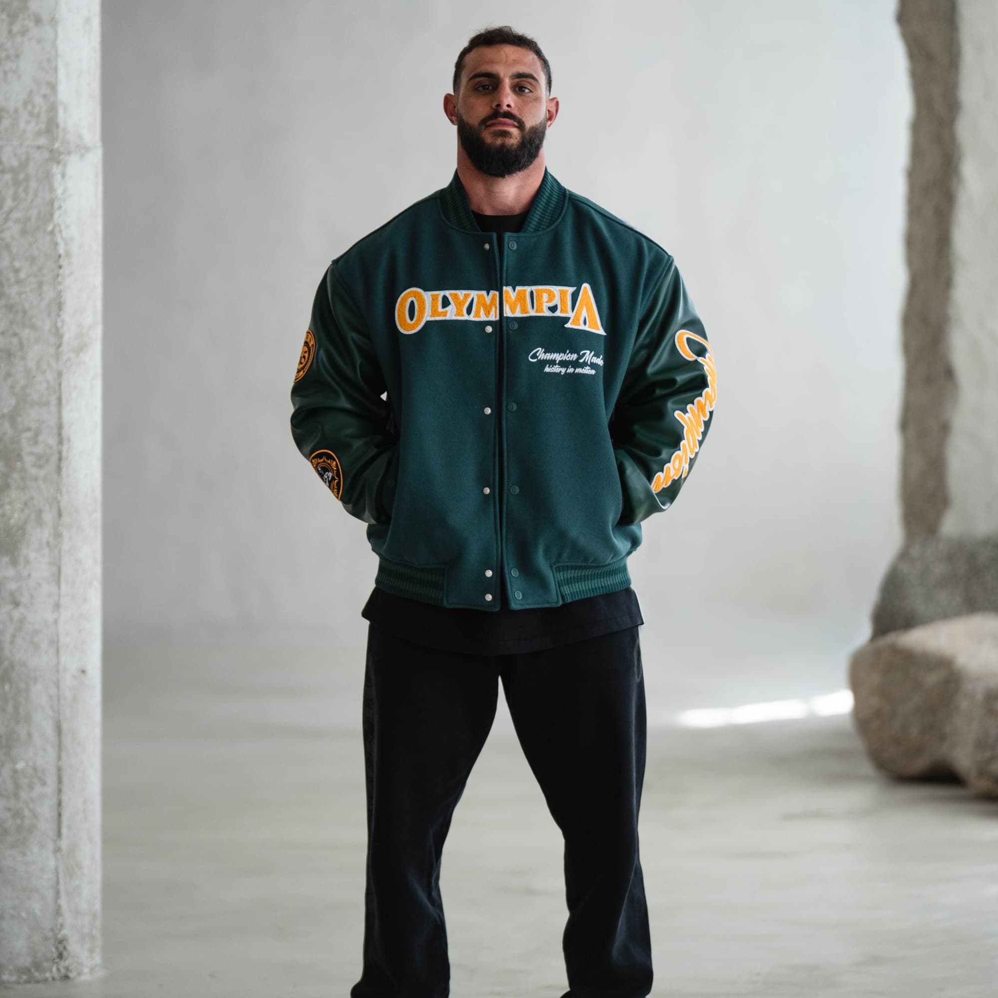 Front view of green Olympia Champion Made Varsity Jacket with gold “Olympia” chest embroidery and white “Champion Made, history in motion” detail.