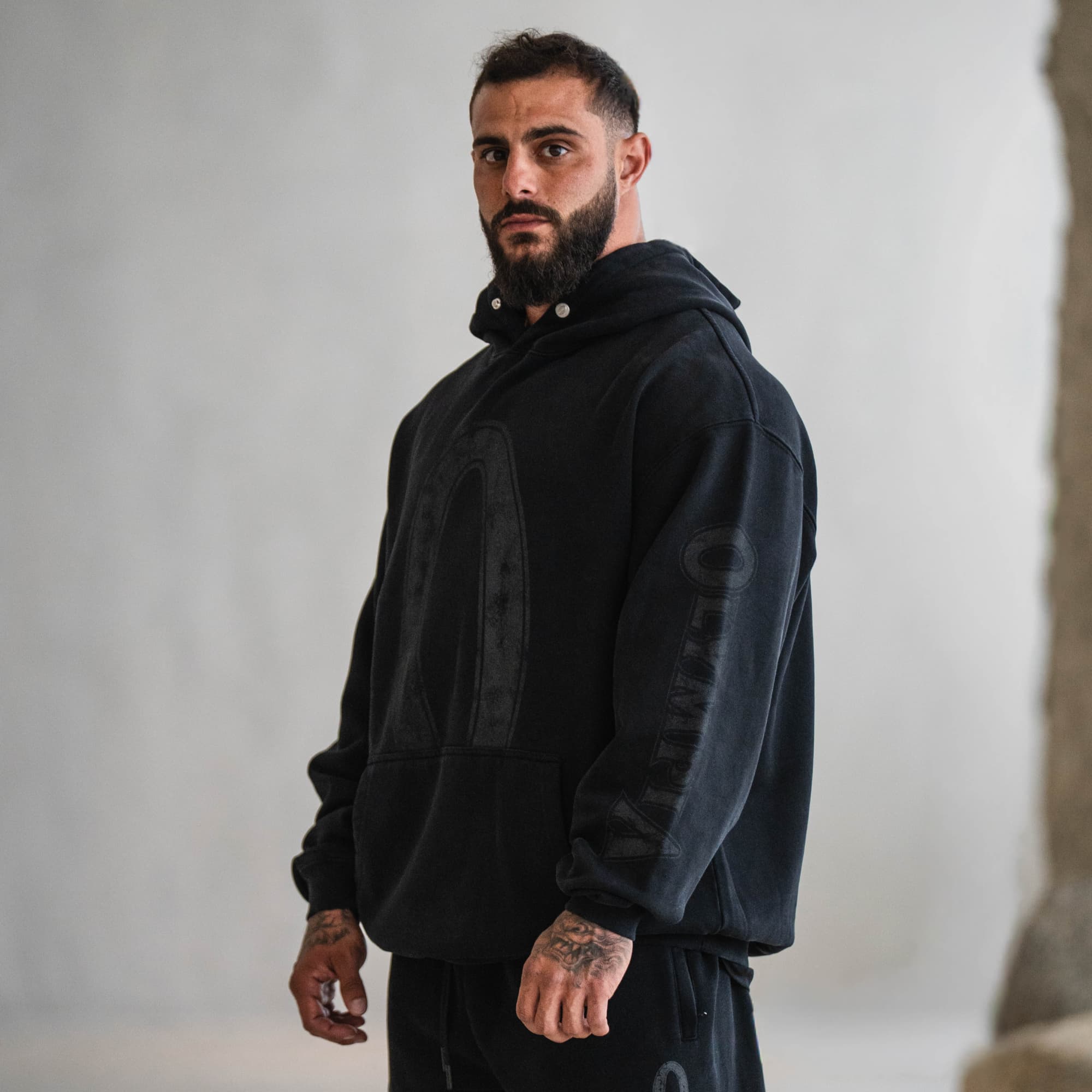 Male athlete wearing the Olympia hoodie in black, featuring oversized “O” graphic and Olympia branding on the sleeve.