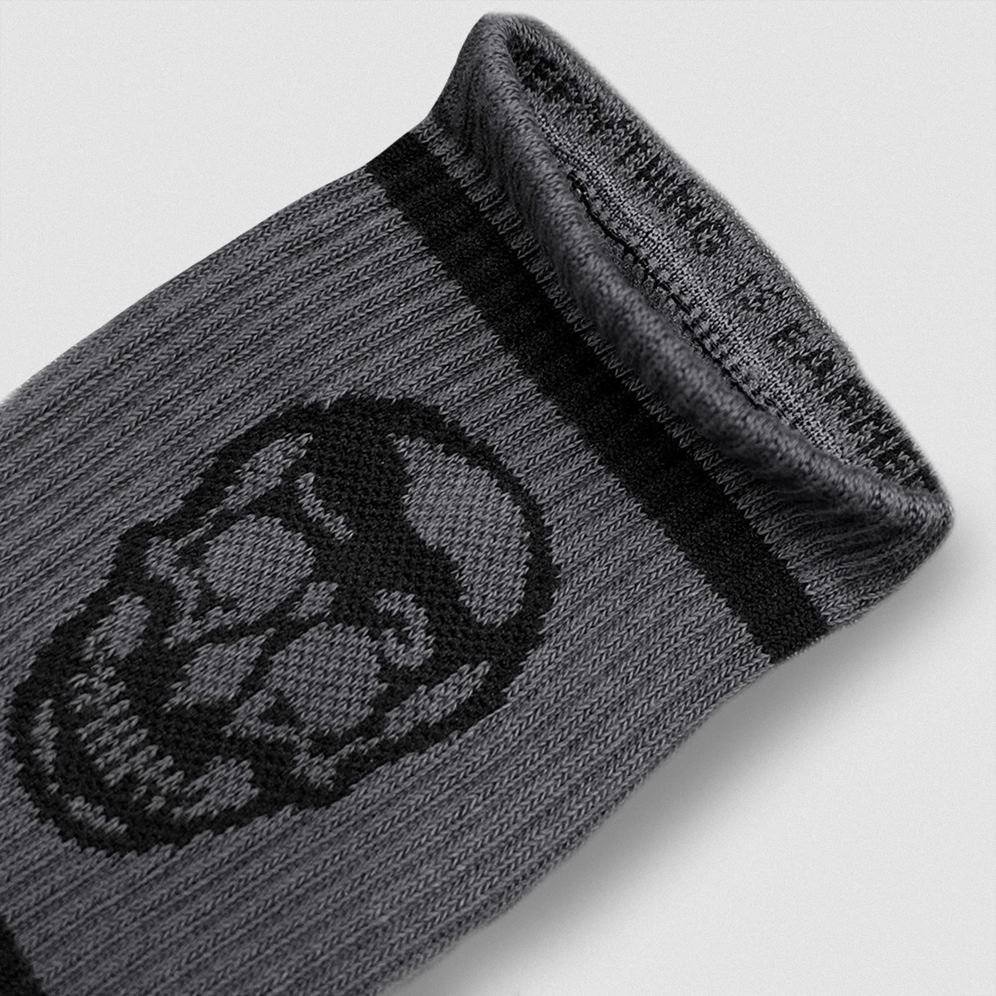 Close-up of a gray Gymreapers wristband featuring a black skull design and woven mantra along the inner cuff.
